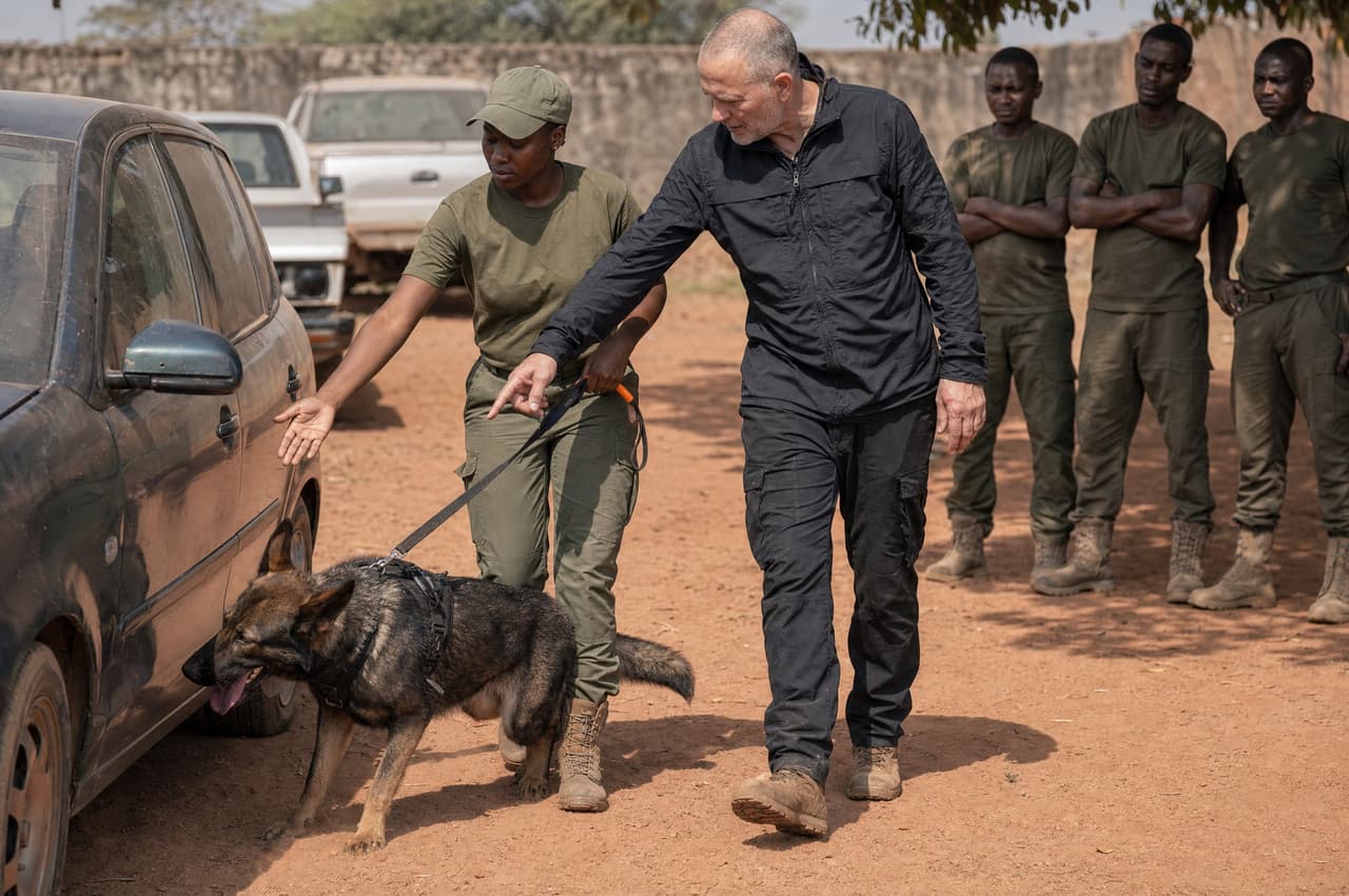 Field training: a trainee leads a German Shepherd along a vehicle, guided by her instructor.